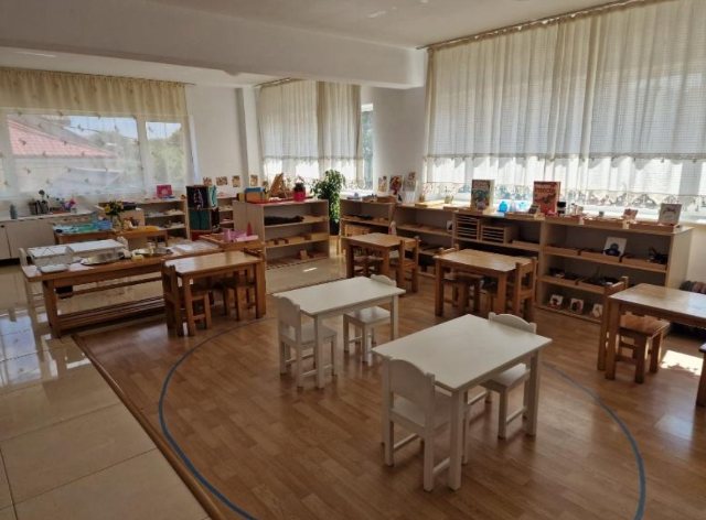 Sala grupei 3–6 ani, cu mese joase din lemn și rafturi cu materiale Montessori